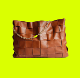 Bolsa feminina de couro na cor marrom, com cortes quadrados, e alça dourada em formato de corrente com detalhe verde, em fundo verde limão